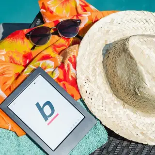 A sunhat, sunglasses, and a reading tablet poolside during summer.