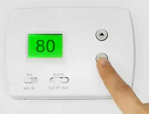 A homeowner adjusting the settings on the furnace thermostat.